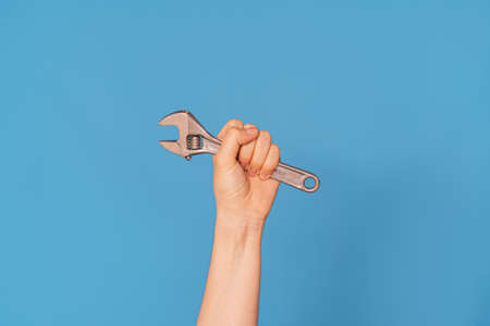 Womans hand with an adjustable wrench against blue backgroundの写真素材