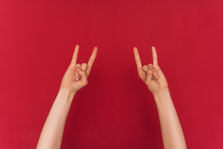 Female hands show rock and roll symbol against red backgroundの写真素材