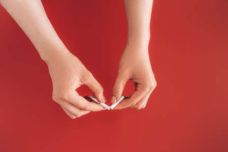 Hands breaking cigarette in half against red backgroundの写真素材