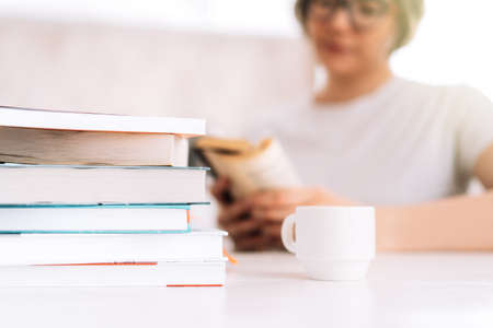 Girl with glasses reading book at table with cup of coffeeの写真素材
