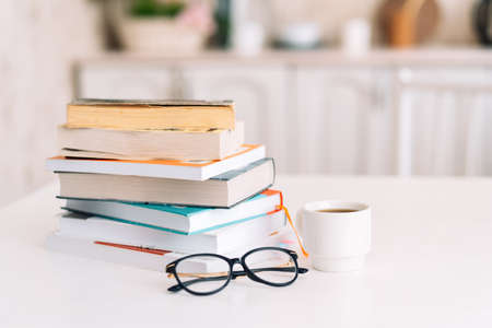 Stack of books with glasses and cup of coffee standing on table