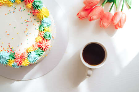 Easter cake decorated with multi-colored cream next to tulips and coffeeの写真素材