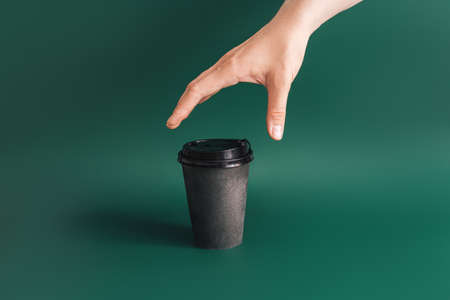 Hand reaching for dark cup on green backgroundの写真素材