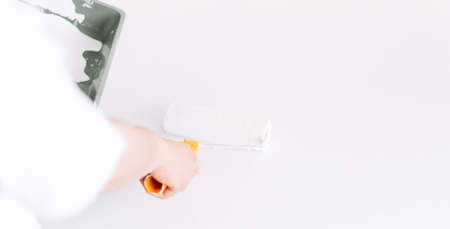 Girl paints the table with white paint the wall with roller