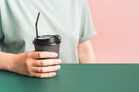 Girl with dark cup in her hands sits at green table against pink background