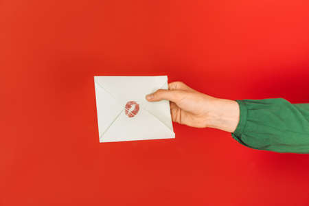 Hand holds out an envelope with kiss mark against red background