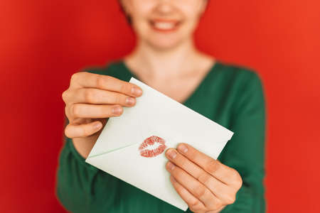 Girl holds in front of her an envelope with trace of kiss against red background