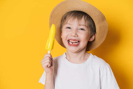 Laughing boy in hat holding rocket-shaped ice cream against yellow backgroundの写真素材
