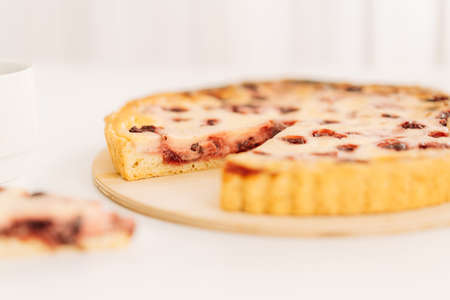 Piece cut from whole cherry pie on wooden board on pink background