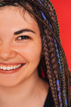Girl smiling with multi-colored pigtails sitting on a white chair against a red backgroundの写真素材
