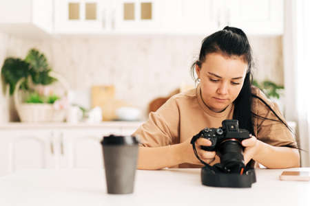 Girl adjusts the camera sitting at a white tableの写真素材