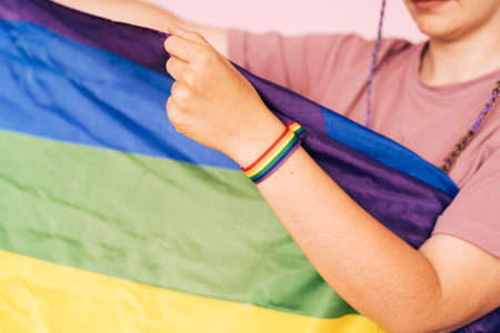 Girl with an LGBT bracelet on her hand holds a rainbow flagの写真素材