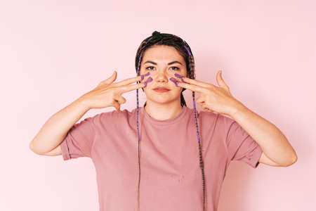 Girl paints with fingers purple paint on her face against a pink backgroundの写真素材