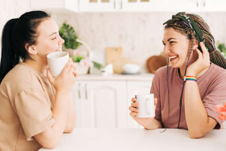 Two girls are talking while sitting at the table in the kitchen drinking a drinkの写真素材