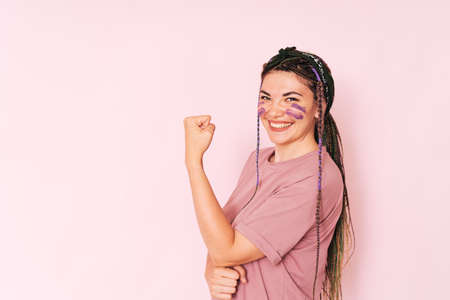 Laughing girl with purple paint on her face clenching her fist against a pink backgroundの写真素材