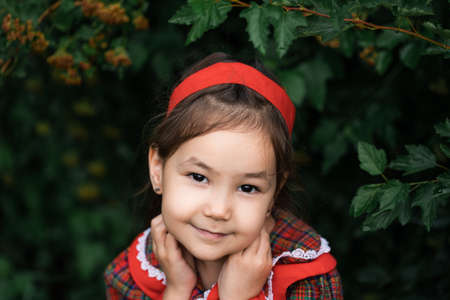 Little girl in a dress in front of green leavesの写真素材