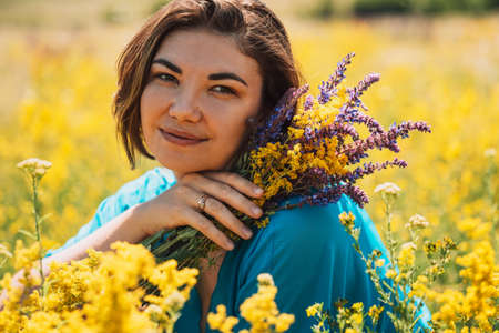 Girl holding ginseng in her hands sitting on field of blooming bedstrawsの写真素材
