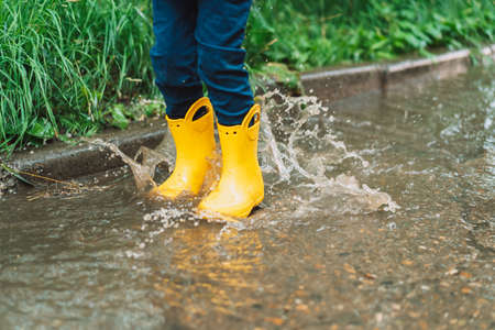 Boy in yellow rubber boots jumping in puddlesの写真素材