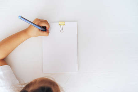 The child writes with a pen on a stack of paper fastened with a clothespin