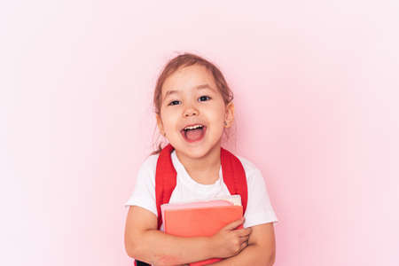 Little girl with a red briefcase with books in her hands against a pink backgroundの写真素材