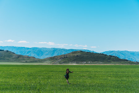 Girl in green dress with hat in her hands walks along feather grass field