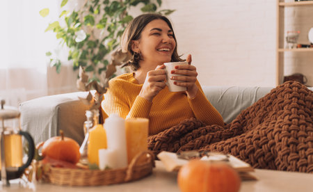 Lady drinks herbal tea brewed in a teapot in front of burning candles and a pumpkinの写真素材