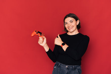 Lady holding gamepad in her hand against red backgroundの写真素材