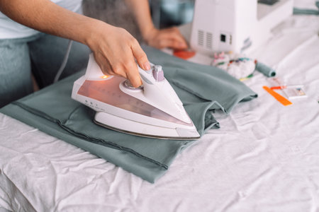 Lady steam ironing the fabric in front of the sewing equipmentの写真素材