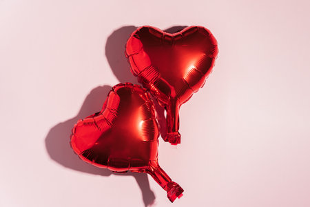 Two red balloon in the shape of a heart on a pink backgroundの写真素材