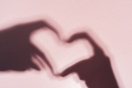 Shadow in the shape of a heart from the hands on a pink backgroundの写真素材