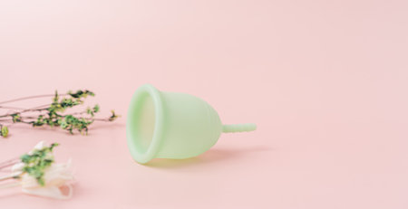 Green menstrual cup on a pink background next to dry plantsの写真素材