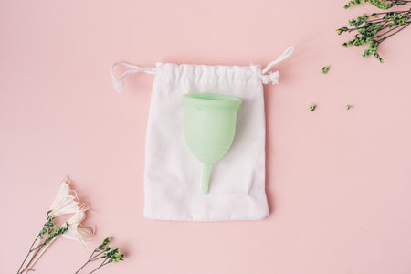 Green menstrual cup on white pouch next to dry flowers on pink backgroundの写真素材