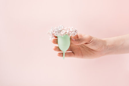 Menstrual cup with small white flowers in a female hand against a pink backgroundの写真素材