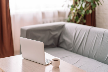 Laptop with a white cup of coffee on the table in front of the sofaの写真素材