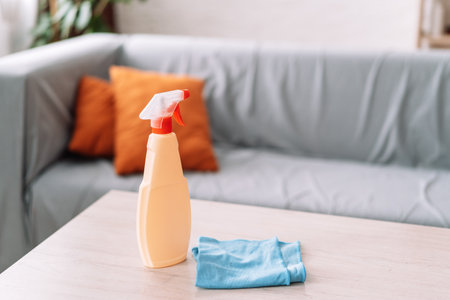 Spray with detergent and blue rag on the table opposite the sofaの写真素材