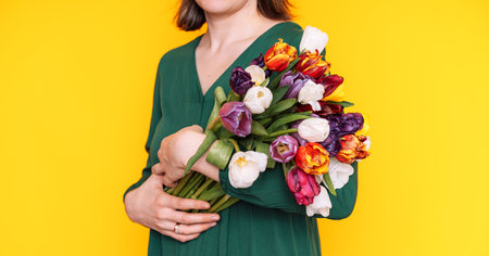 Lady in a green dress with a large bouquet of tulips in her hands against a yellow backgroundの写真素材