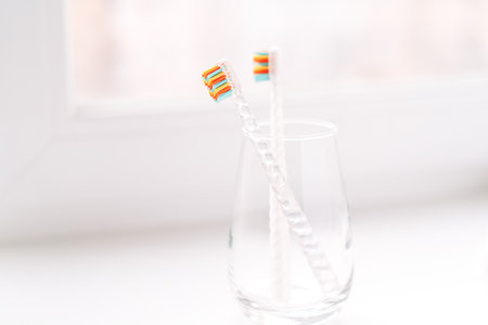 Childrens toothbrushes in a glass cup on the windowsillの写真素材
