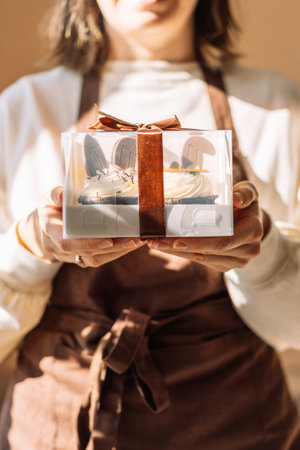 Lady pastry chef in brown apron holding box of cupcakes with bunny ears