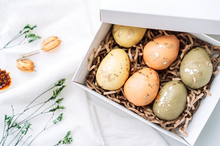 Easter eggs of different colors in box on white background with dried flowersの写真素材