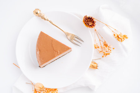Chocolate cheesecake on plate with fork against white background with dried flowers and napkinの写真素材