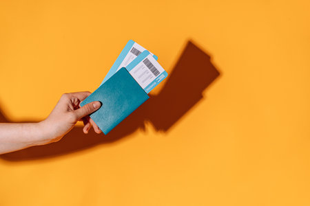Tickets in passport in hand against yellow background under yellow light