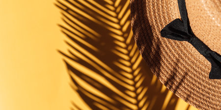 Shadow of palm branch falls on straw hat against yellow background