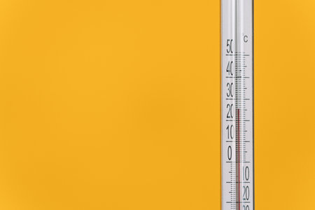An outdoor thermometer with a mark of twenty-five degrees Celsius against yellow background