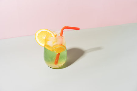 Glass cup with straw with citrus drink with ice against pink backgroundの写真素材