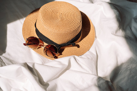 Sunglasses and hat on white bed under the sunbeamsの写真素材
