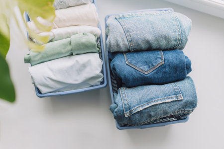 Folded jeans and t-shirts in blue containers on the windowsillの写真素材