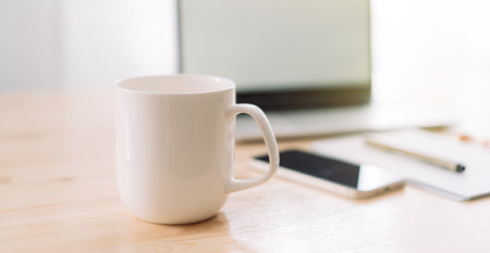 White mug without inscriptions opposite laptop and notepad with pen on wooden tableの写真素材