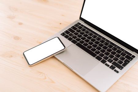 Smartphone and laptop with white screens for text or advertising on wooden tableの写真素材