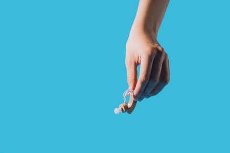 Hearing aid in hand against blue backgroundの写真素材