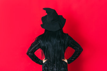 Ledy in witch costume keeps her hands on her hips facing red backgroundの写真素材
